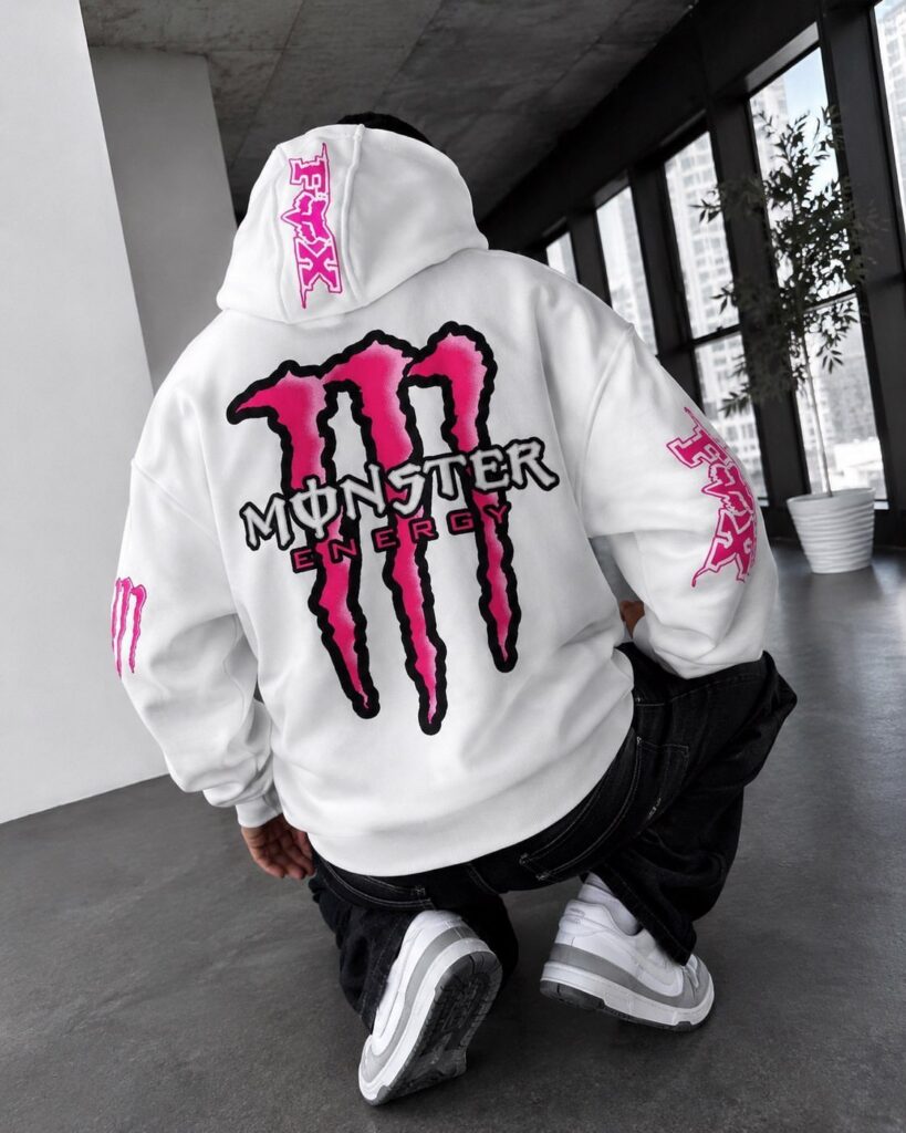Person wearing a white Monster Energy graphic hoodie while crouching in a modern room.