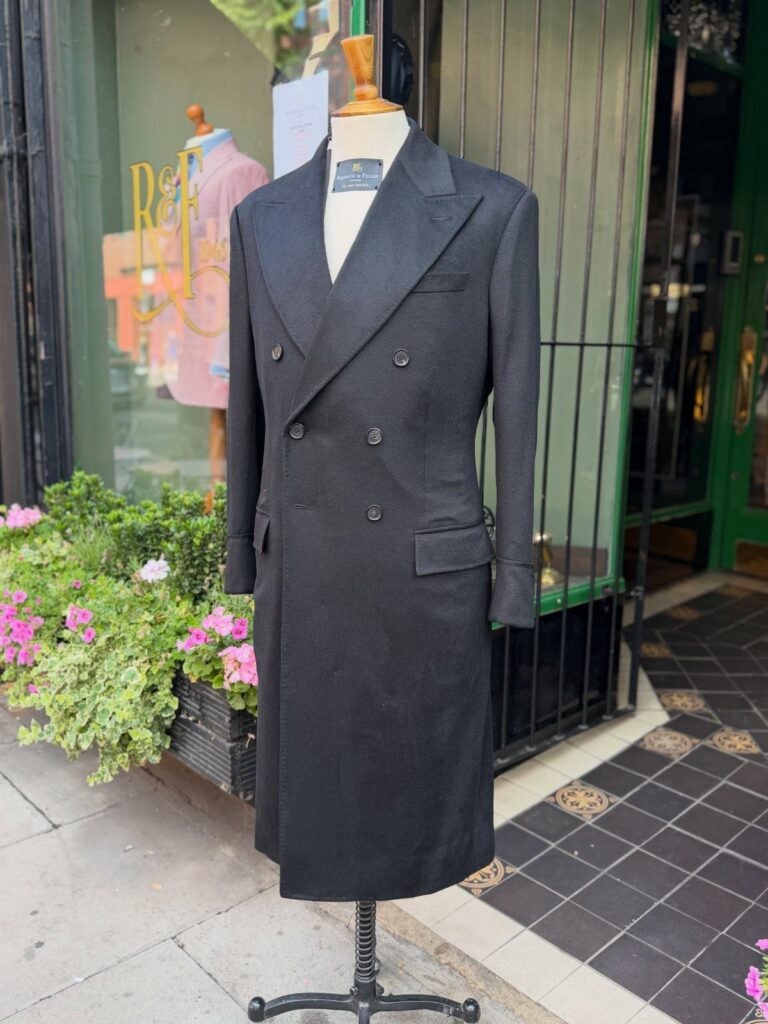 A long charcoal grey double-breasted topcoat with peak lapels on a mannequin.