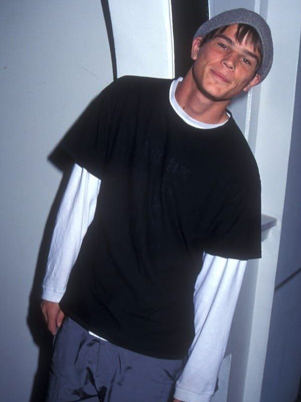 Young man wearing a black t-shirt over a white long-sleeve shirt and a grey beanie.