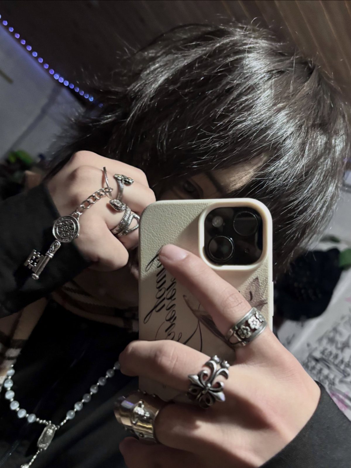 Person with shaggy dark hair wearing many chunky silver rings and a key necklace.