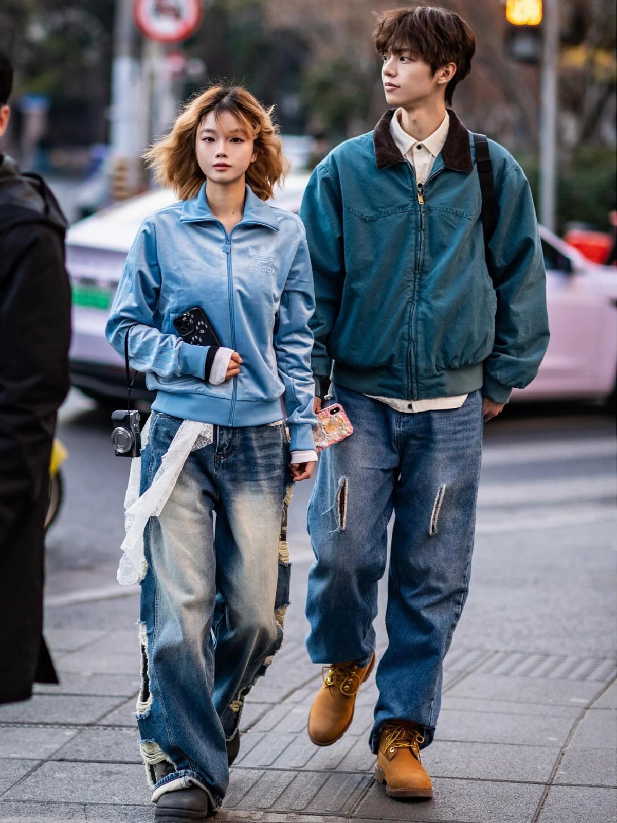 Two young people walking down a city street wearing trendy, oversized denim and casual jackets.