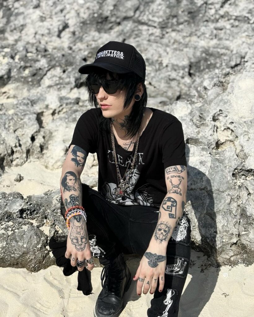 A person in alternative fashion wearing a black graphic t-shirt and black skinny jeans outdoors.