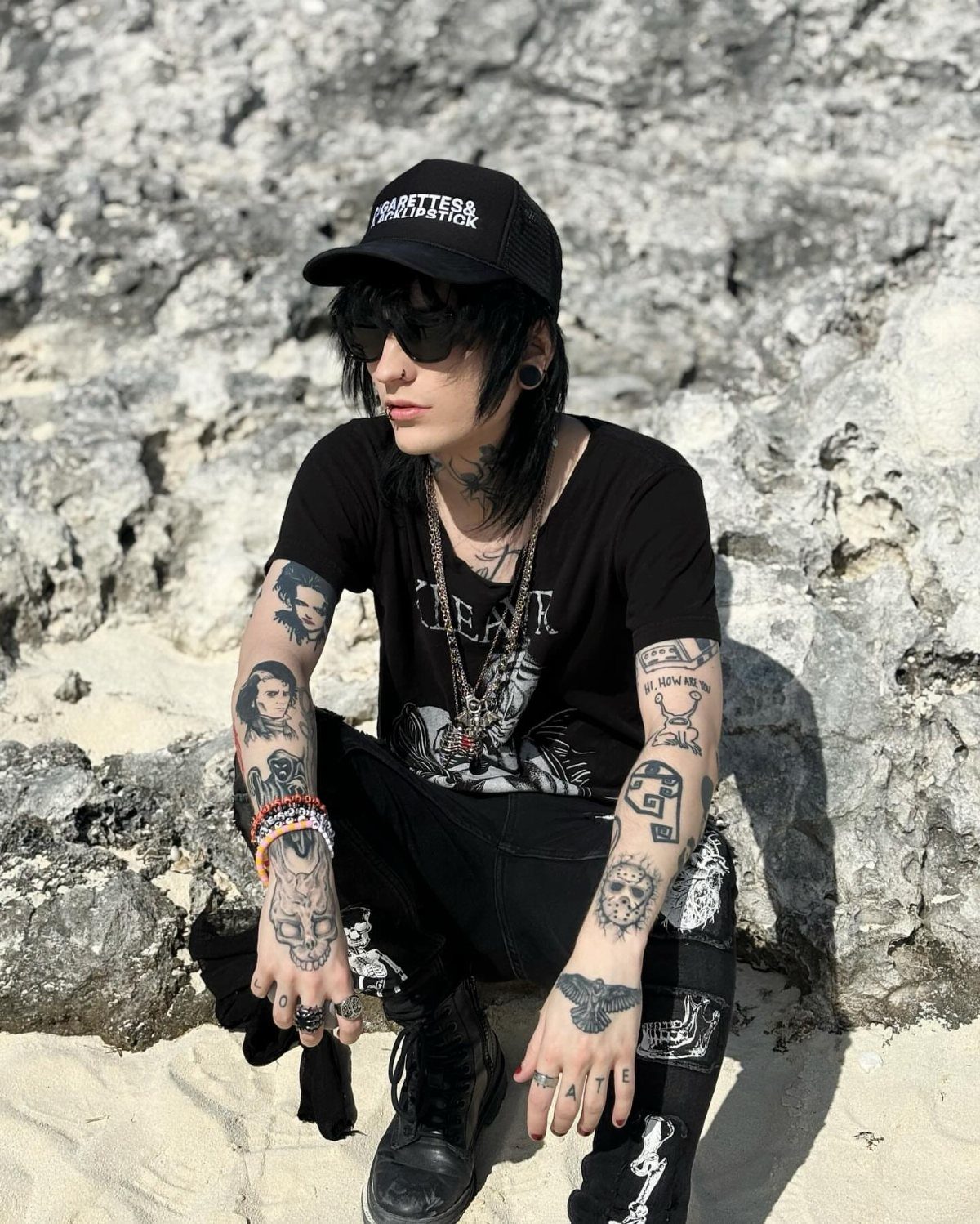 A person in alternative fashion wearing a black graphic t-shirt and black skinny jeans outdoors.