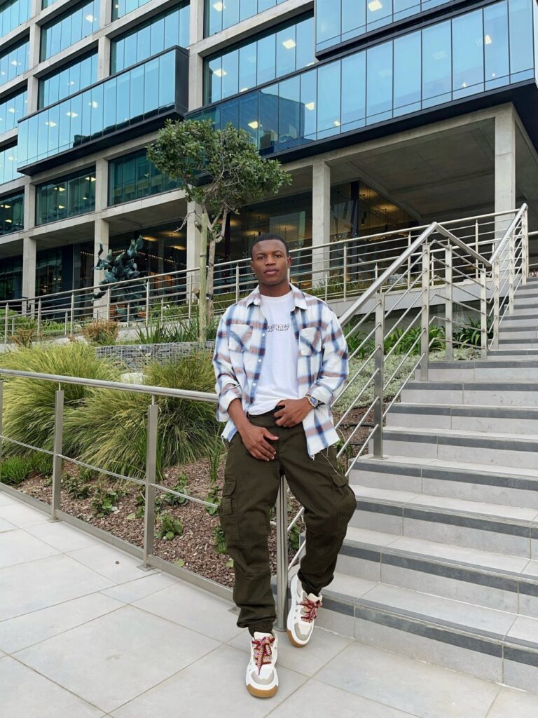 Man sitting on stairs wearing a plaid flannel shirt, white t-shirt, and olive cargo pants.
