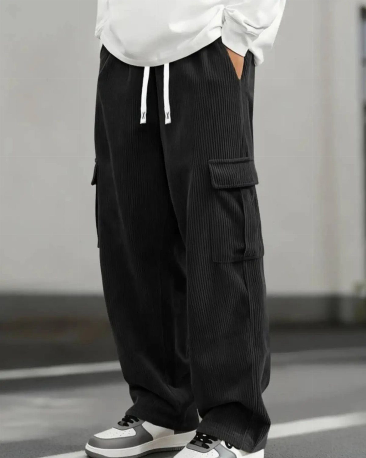 Person wearing wide black corduroy cargo pants with white drawstring and white sneakers.