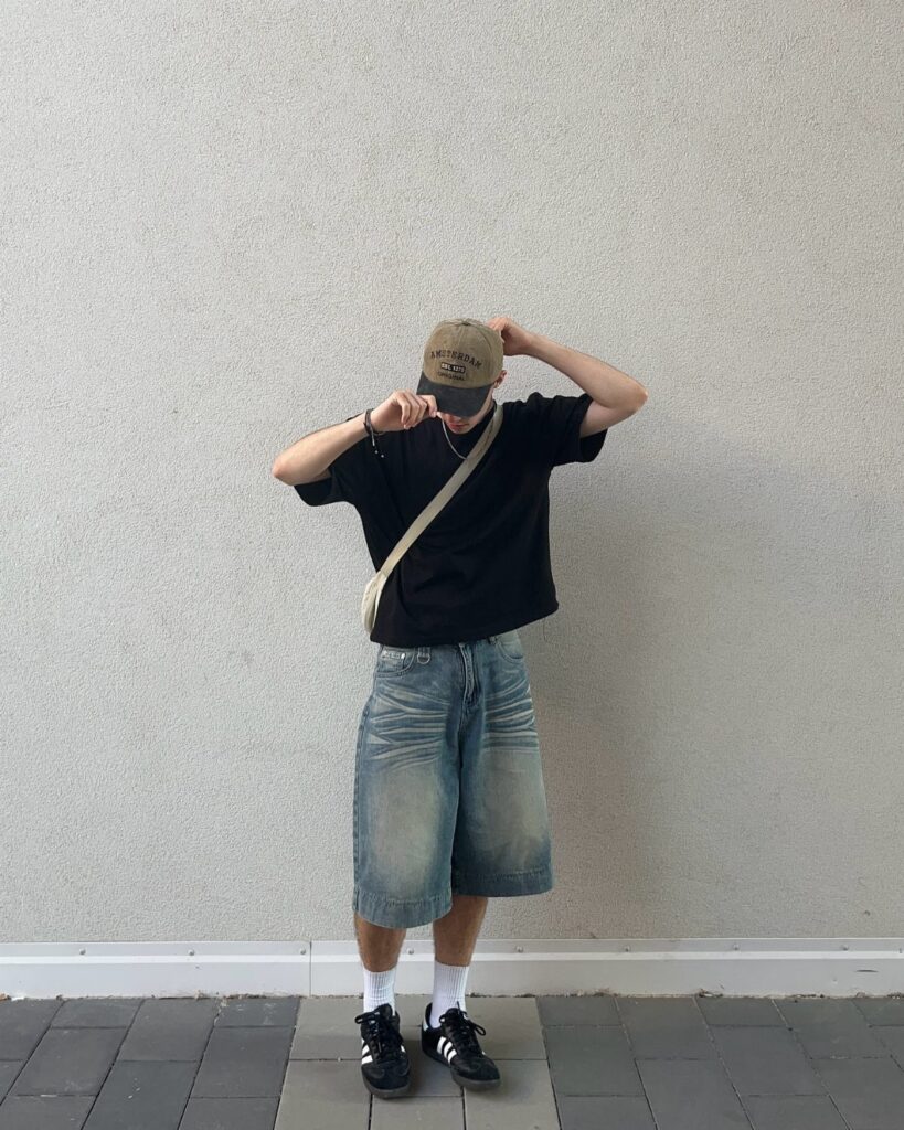 A person wearing a black t-shirt, baggy denim shorts, white socks, and black sneakers.
