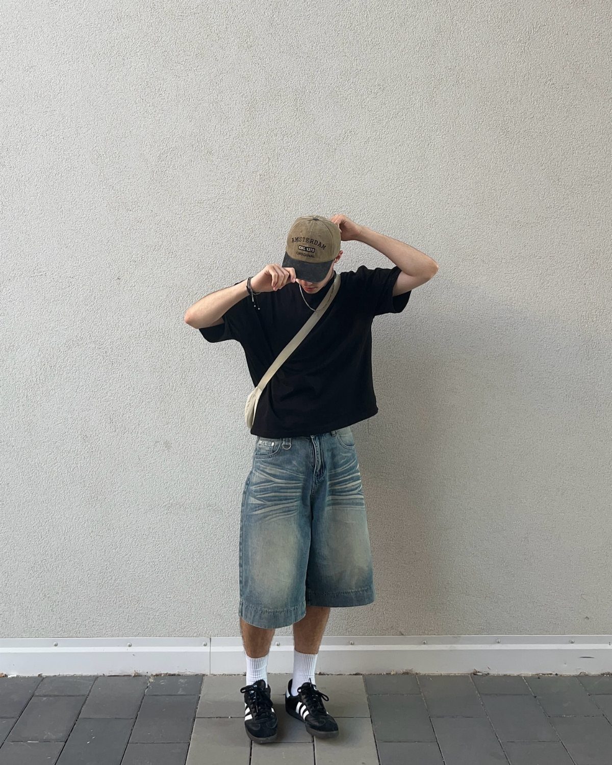 A person wearing a black t-shirt, baggy denim shorts, white socks, and black sneakers.