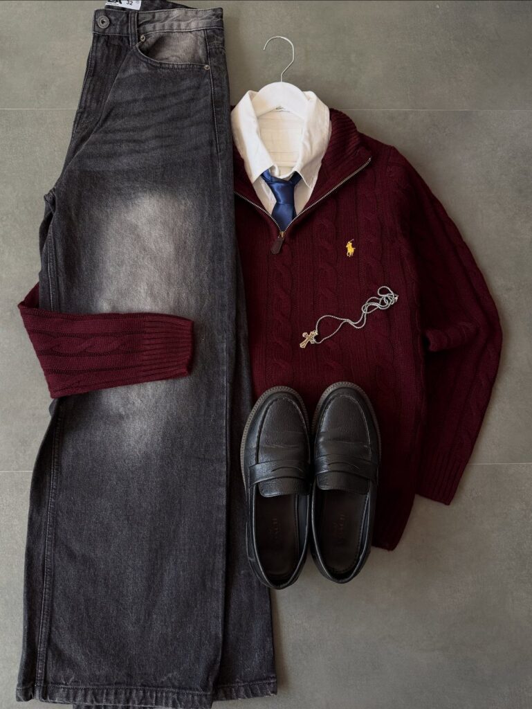 Burgundy cable knit sweater, white shirt, blue tie, grey trousers, and black loafers laid out.