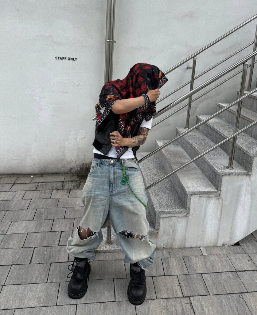 Person wearing baggy light-wash distressed denim jeans with knee rips and black combat boots.