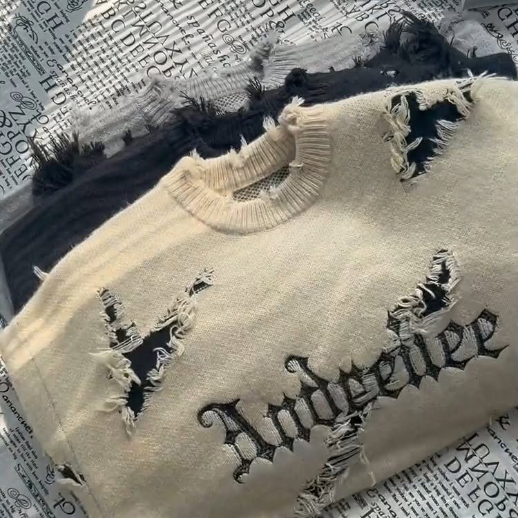 Distressed cream and black sweaters with ripped holes and gothic lettering on newspaper print.