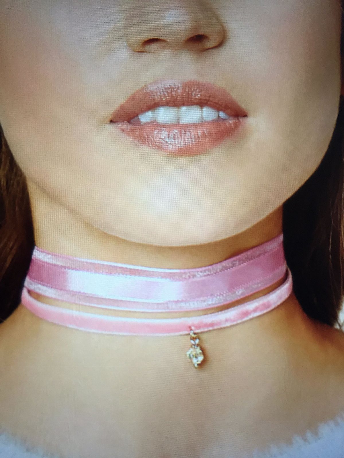 Pink velvet choker with a small crystal pendant worn around a person's neck.