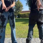 Two people standing in a sunny yard wearing black graphic tees and patterned denim jeans.