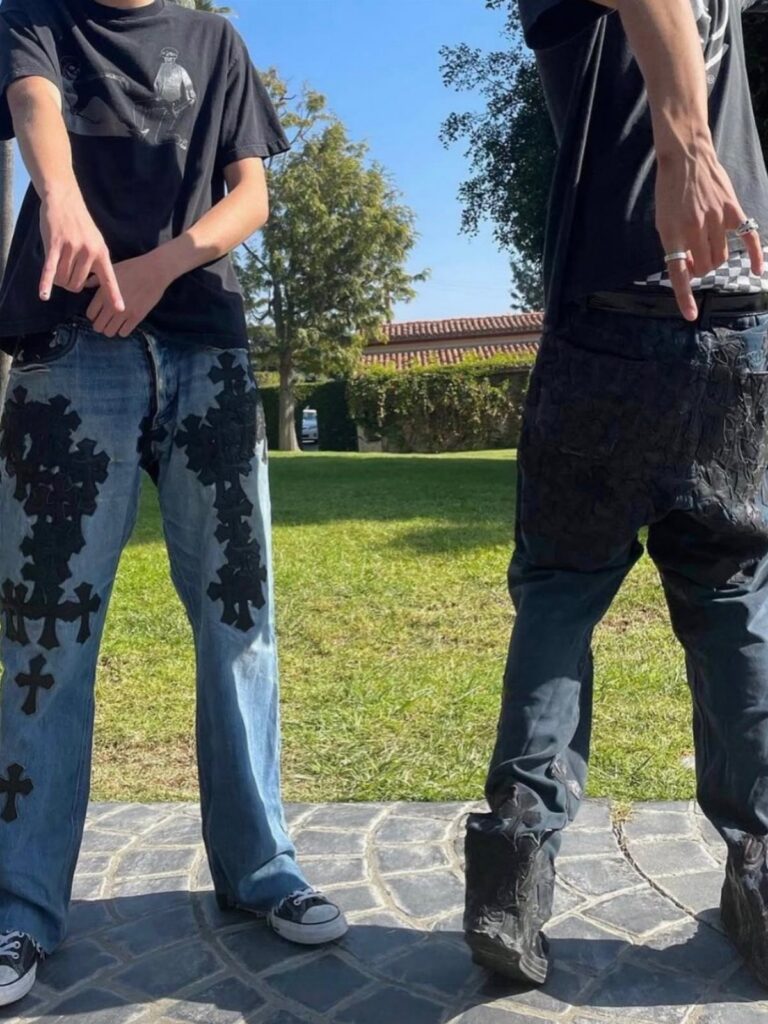 Two people standing in a sunny yard wearing black graphic tees and patterned denim jeans.