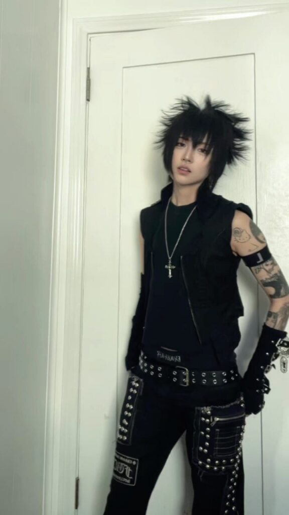 Person with spiky black hair wearing a studded black punk and emo fusion outfit.