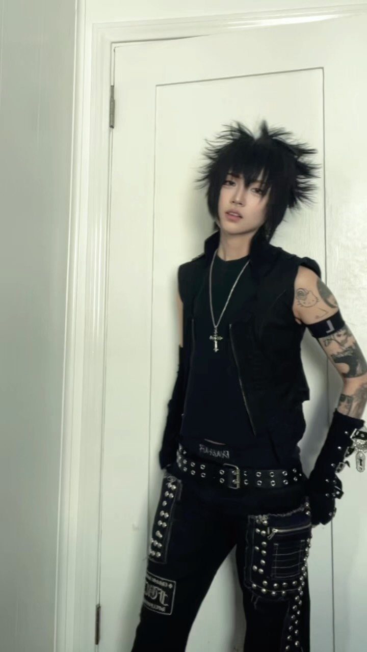 Person with spiky black hair wearing a studded black punk and emo fusion outfit.