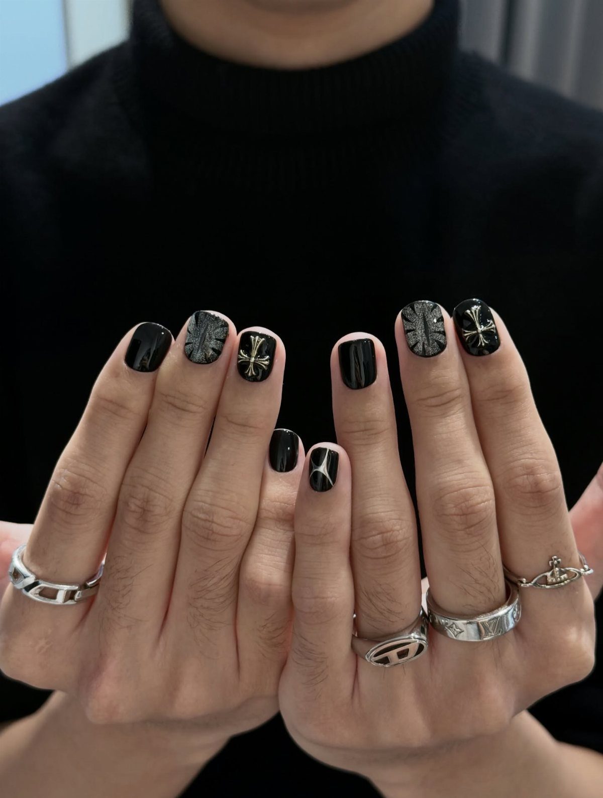 Hands with black manicured nails featuring silver cross and textured designs and silver rings.