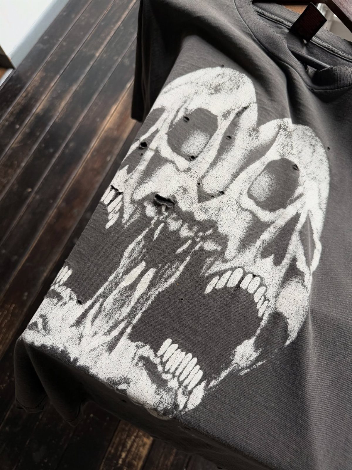 A dark grey t-shirt with a large, distressed white graphic of two screaming skulls.