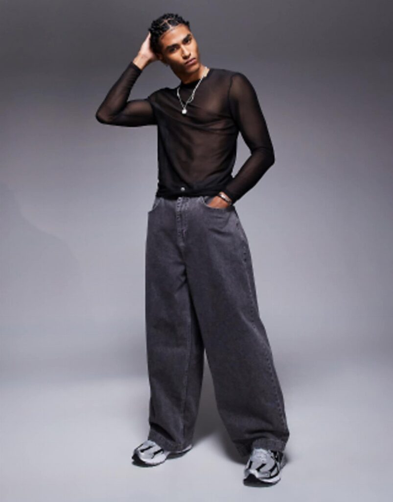 A man wearing a black mesh long-sleeve top and dark grey wide-leg trousers.