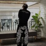 Person from behind wearing black Ed Hardy sweatshirt and graphic patterned pants standing in a room.
