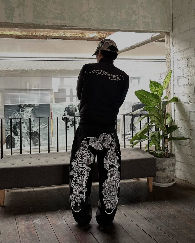Person from behind wearing black Ed Hardy sweatshirt and graphic patterned pants standing in a room.