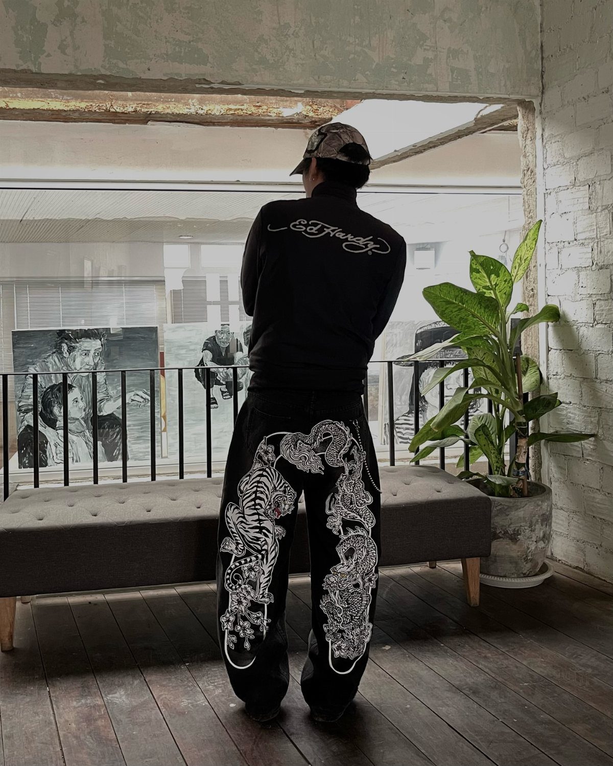 Person from behind wearing black Ed Hardy sweatshirt and graphic patterned pants standing in a room.