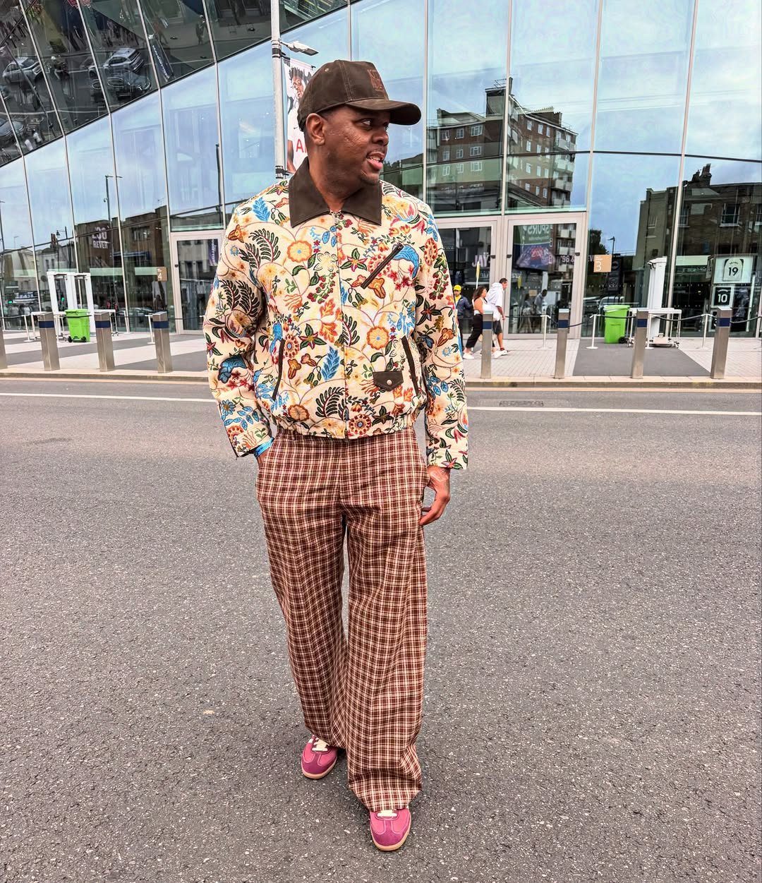 A man wearing a patterned jacket and brown plaid trousers standing on a city street.