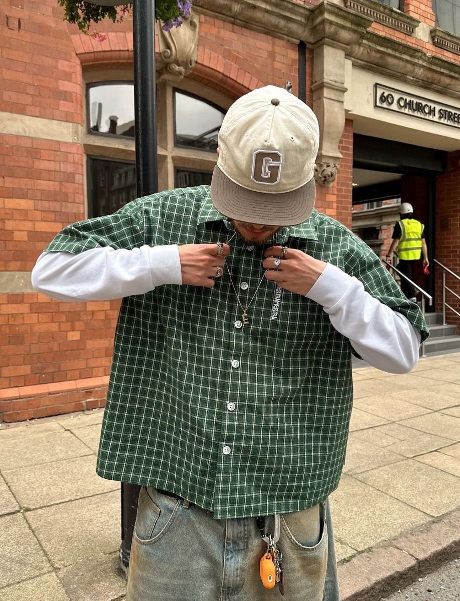 Person wearing a green checkered shirt over a white long-sleeve shirt and light blue jeans.