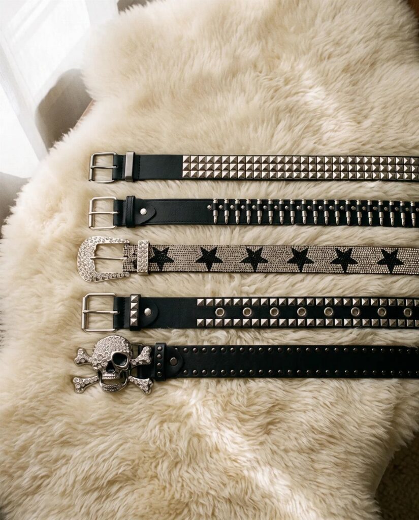 Five black studded and decorated belts resting on a white fluffy faux fur background.