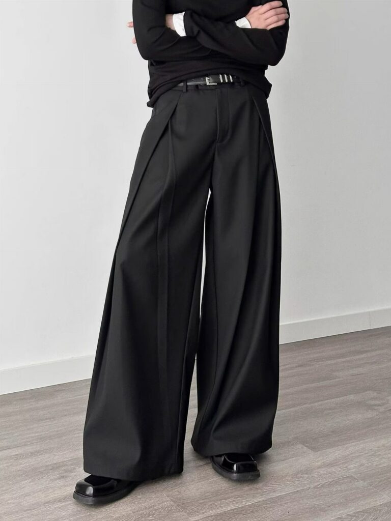 Person wearing black high-waisted wide-leg pleated trousers and a black long-sleeved shirt.