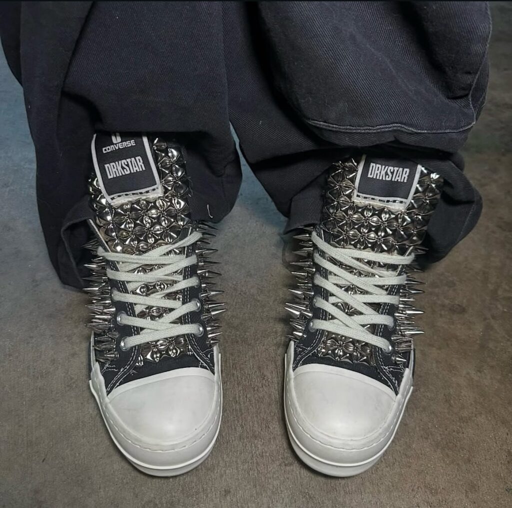 Black high-top sneakers covered in silver metal spikes and studs worn with dark pants.