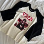 A white and black long-sleeved shirt with a red graphic print lying on white fabric.