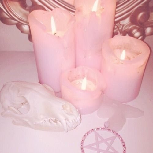 Pink lit candles, a white animal skull, and a pentagram charm on a pink surface.