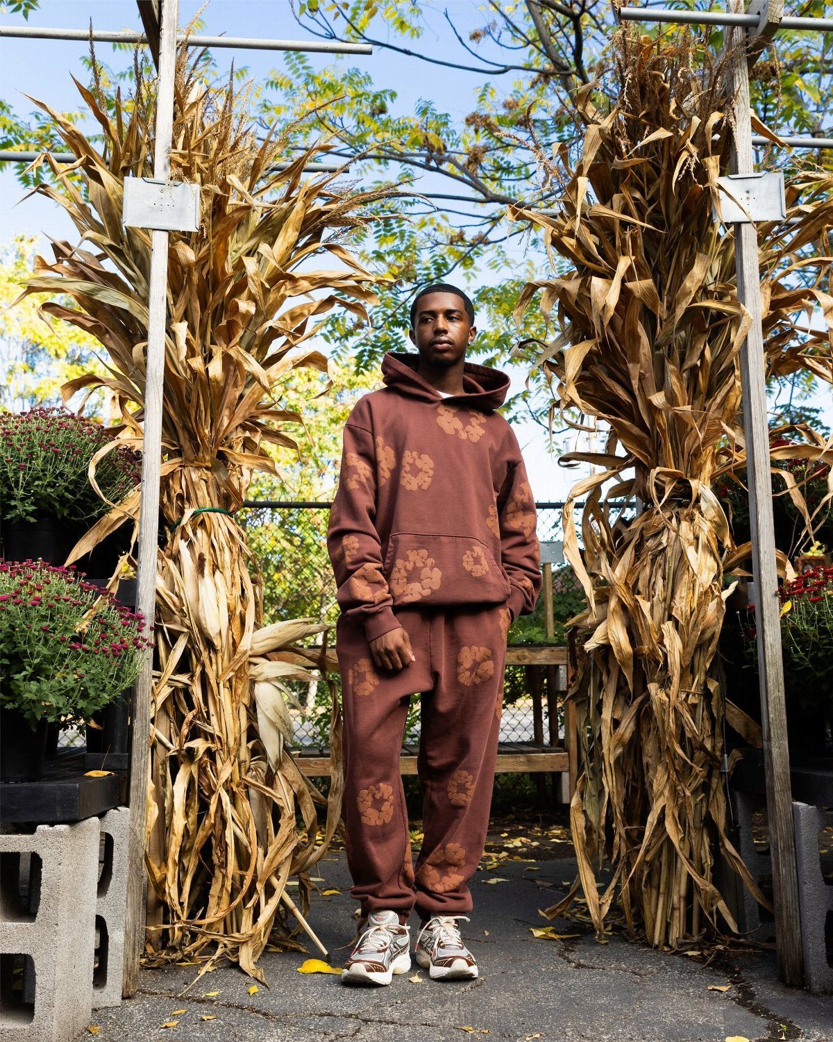Man in a matching brown floral print hoodie and sweatpants standing between dried corn stalks.