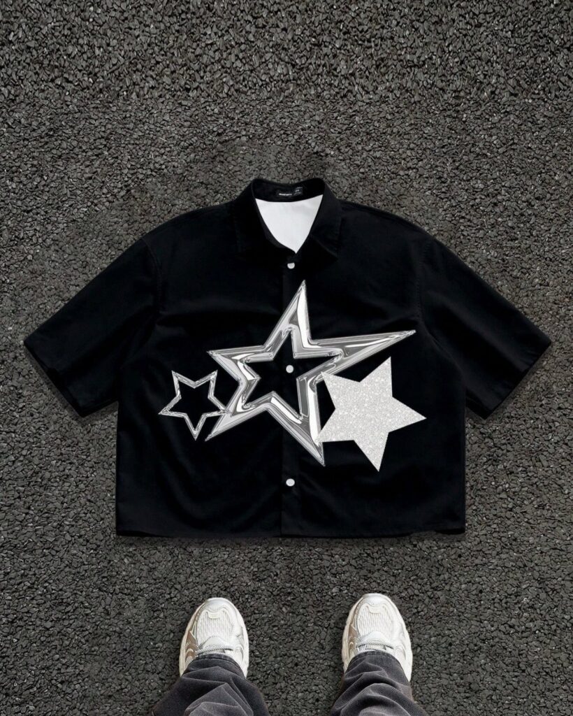 Black short-sleeved shirt with large silver star graphics lying on dark asphalt pavement.