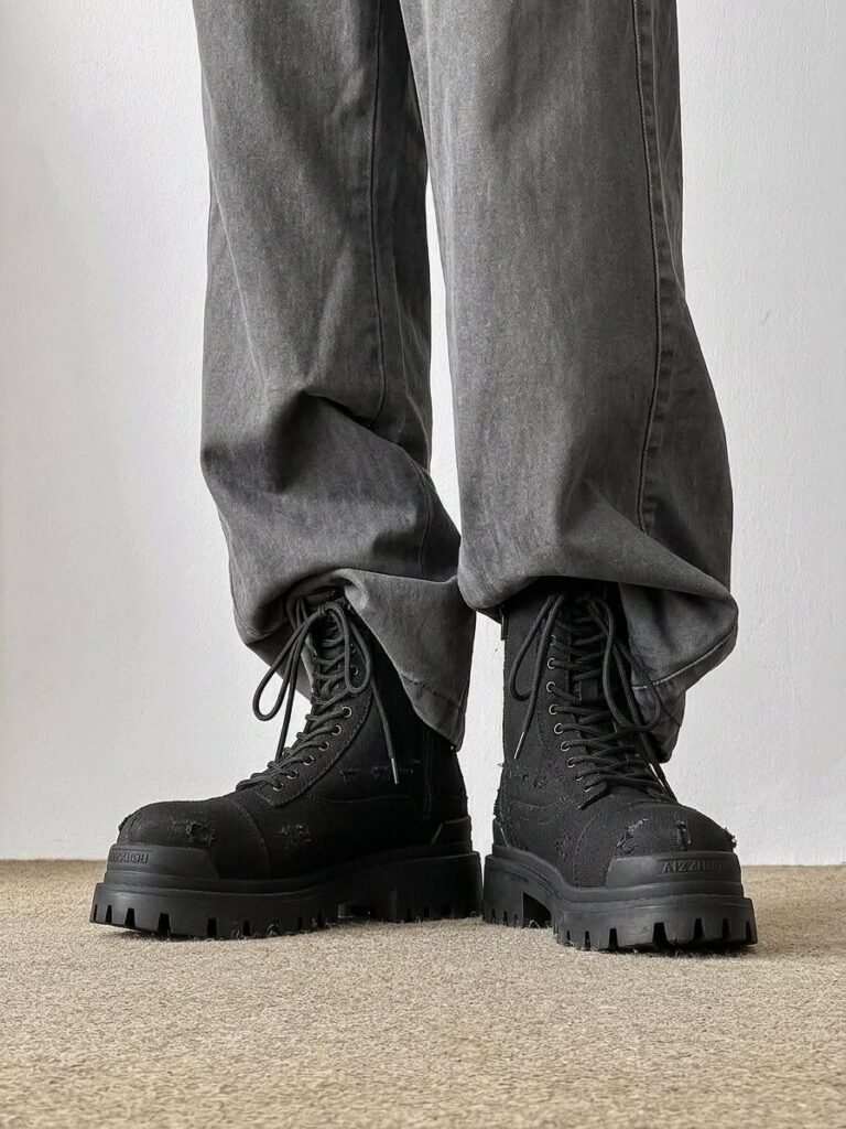 Black platform combat boots with thick lug soles worn with baggy grey denim pants.