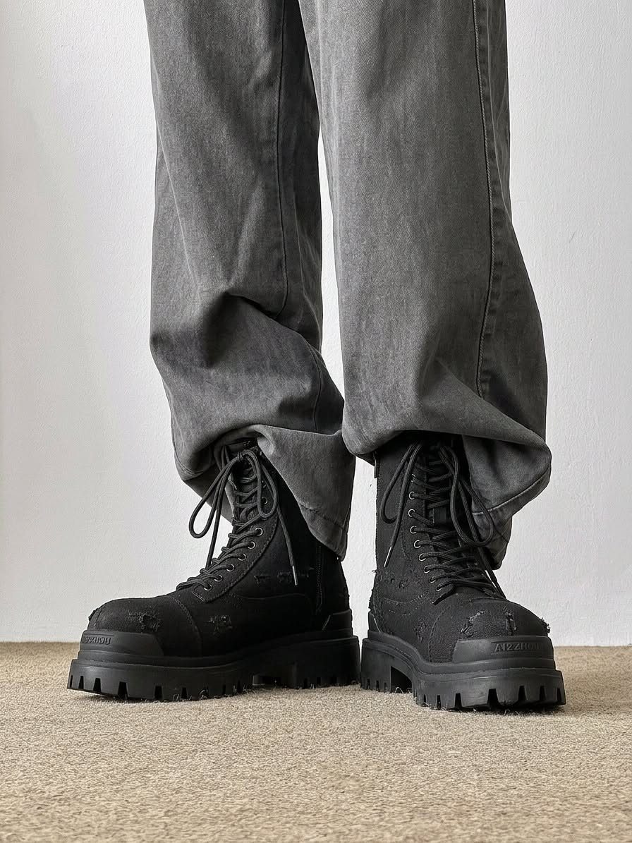 Black platform combat boots with thick lug soles worn with baggy grey denim pants.